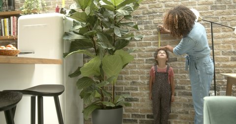 Mother measuring daughter’s height at home, milestone, growth, parenthood, single mother