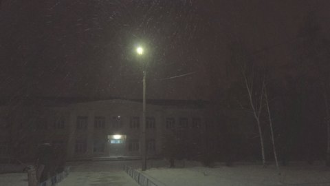 Falling snow or a blizzard under a street lamp at night in front of the entrance to a two-story building