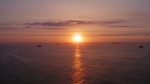 Cargo and fishing vessels are anchored in the roadstead. Beautiful sunrise on the horizon. Silhouettes of ships