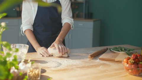 Successful Businesswoman is Happy To Knead the Dough on a Wooden Table in a Cozy Home Kitchen. Woman Baker Enjoys the Process of Making Homemade Cakes. Favorite Work. Small Business.
