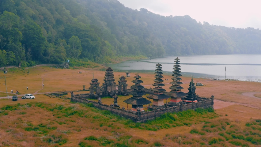 Ancient Balinese temple with traditional architecture located at the foot of the natural volcanic Tamblingan Lake. Bali, Indonesia. 4K Aerial 