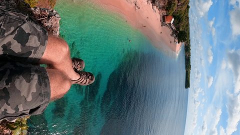 Awesome first person view active lifestyle people sitting on top mountain cliff on background beach and azure clear ocean at sunny day. 4K Vertical UHD Video Clip