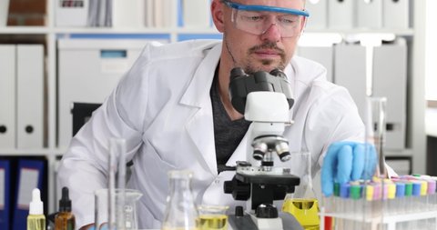 Scientist chemist wearing glasses holding test tube with blood and looking microscope 4k movie