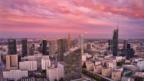 Fly forwards above downtown skyscrapers in sunset time. Hyperlapse footage of city centre. Dimming pink sky changing colour to blue. Warsaw, Poland