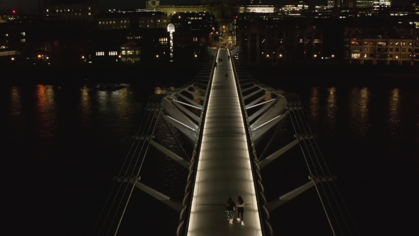 Fly above modern designed Millennium Footbridge across Thames river. Tilt up reveal of Saint Pauls Cathedral. London, UK