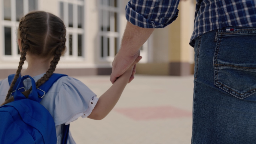 father holds happy daughter by the hand, accompany little child with backpack to school, study in preschool preparation, walk through schoolyard, first grade student with school bag on his shoulders Royalty-Free Stock Footage #1080710978