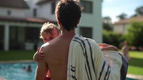 Back of father holding baby infant boy in arms at swimming pool outdoors. Dad bonding with toddler son