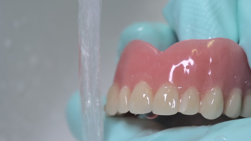 Closeup shot showing brushing of dentures with running water. Rubber gloves used for hygiene. Royalty-Free Stock Footage #1080713306