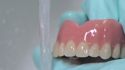Closeup shot showing brushing of dentures with running water. Rubber gloves used for hygiene.