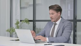 Middle Aged Man Talking on Video Call on Laptop in Office