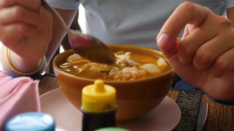 Female Eats tom yum or tom yam soup. Boiled potatoes and noodles on garden outside in summer. Hot and sour Thai soup cooked with shrimp or prawn. Fragrant spices and herbs generously used in broth