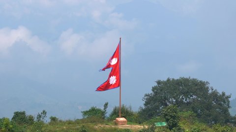 A view of a big Nepal Flag on the top of a hill blowing in the wind. 