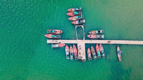 Asian fishing boats with workers preparing for a trip, moored on a pier in wobbling in ocean currents of the emerald green sea water. Aerial drone birds eye time lapse.