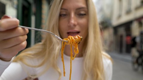 Beautiful blond woman eating pasta bolognese at street restaurant