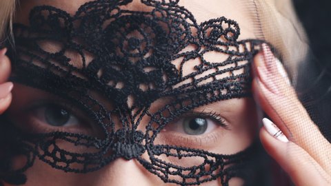 Blond woman with Venetian black mask red lipstick and black veil. Close up on green eyes