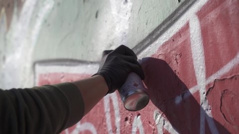 Close up shot of a hand wearing black gloves painting graffiti on wall. Artist drawing black line in a grafiti with a spray paint