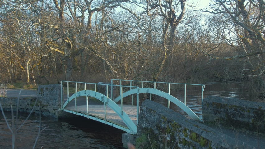 Cyclist crosses walk bridge over river in forest during Winter. WIDE SHOT