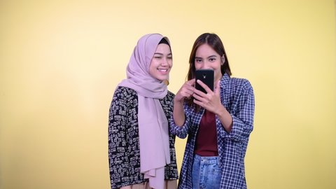 two asian women laughing using a cell phone while looking at the phone screen