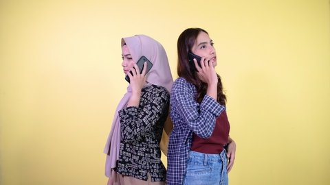 two asian women making phone calls while standing back to back