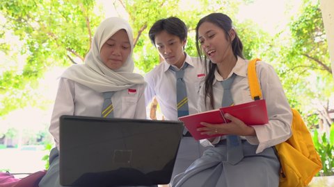 group high school students using a laptop computer and carrying books