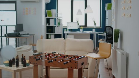 Nobody in workplace for businesspeople meeting after work for drinks and party celebration. Empty office with football game table, snacks and bottles with alcoholic beverage for fun
