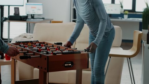 Multi ethnic coworkers playing soccer game at foosball table with drinks after work. Cheerful workmates enjoying football play, beer and snacks to celebrate party at office after hours