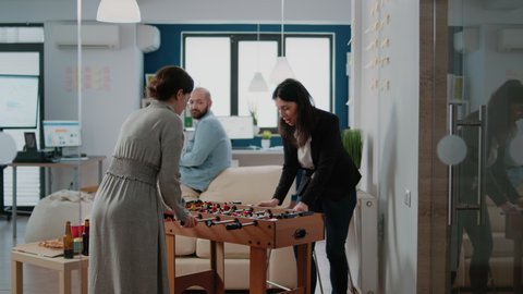 Women playing with foosball game table to have fun after work at office. Coworkers enjoying free time with football and beer drinks to celebrate party with cheerful colleagues after hours