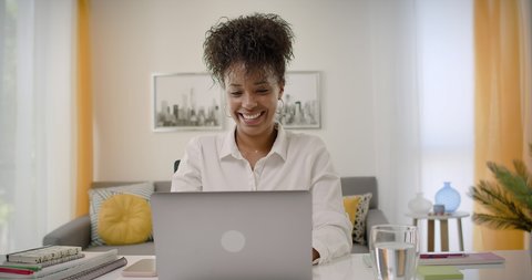 Video Conference Call at Home Office. Lateral Dolly of Happy Young African American Woman Working or Studying on Laptop Computer from Home. Online Learning or Teleworking Concept.
