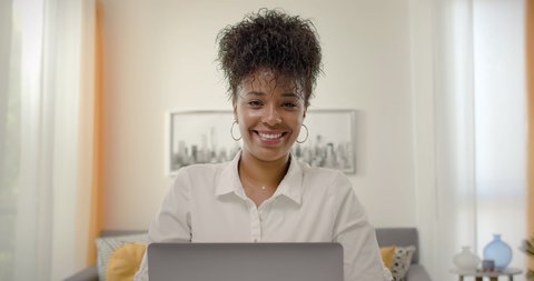 Young Beautiful African American Works on Laptop Computer. Camera Dolly in and She Smiles and Laughs. Teleworking home office.