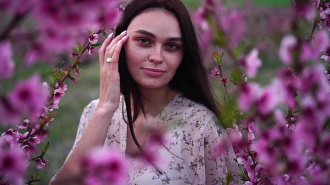 Beautiful brunette girl is in a peach orchard. Pink and purple flowers. Fruit trees blooming Arkivvideo