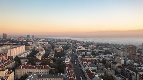 Morning backwards fly above urban neighbourhood. Hyperlapse of cityscape at sunrise, mist rolling in background. Warsaw, Poland