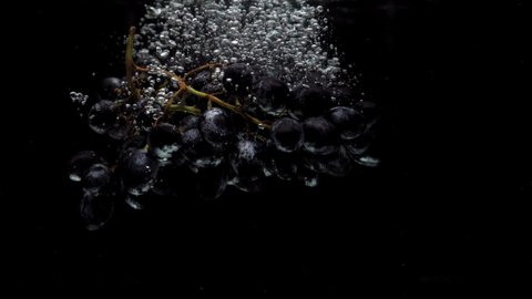 Slow motion blue grapes falling into transparent water on black background. Fresh fruit splashing in aquarium. Healthy food, diet, air bubbles