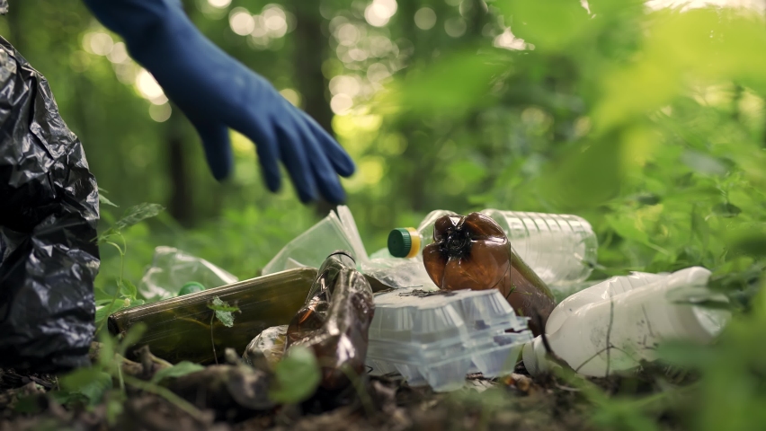 Clean up day. Cropped shot of a young man volunteer wearing uniform and rubber gloves with trash bag in hands cleaning forest or park from garbage. Ecology problems and nature pollution Royalty-Free Stock Footage #1080748736