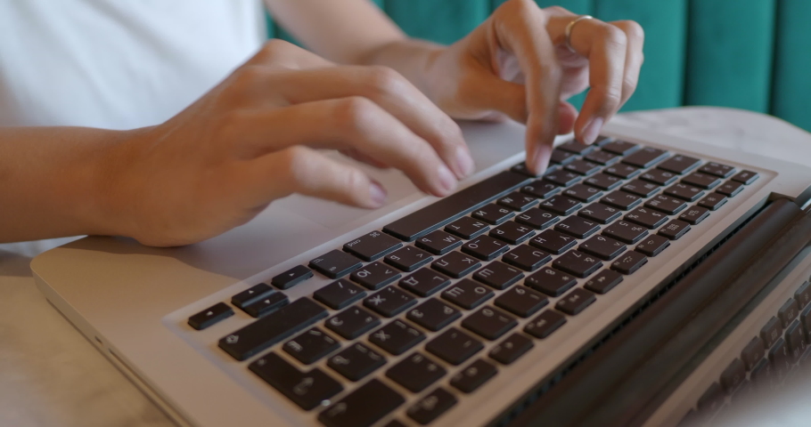 Woman works remotely in cafe with red brick walls. Female types on laptop keyboard. Co-working center with loft interior style. Freelance workplace.