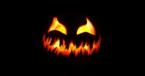 Spooky Halloween jack o lantern with scary face carved out of a pumpkin glowing with flickering light and emitting smoke.