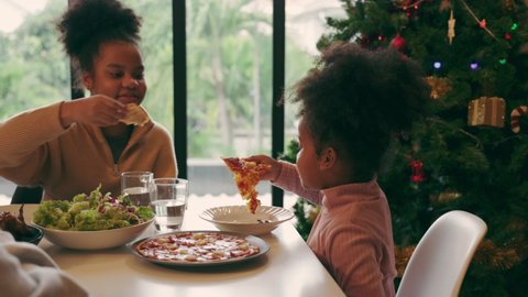 Happy African American family celebrating christmas at home. People having a dinner xmas party eating, talking and smiling. children feed pizza to sister. family relationship स्टॉक वीडियो
