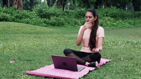 Girl teaching meditation and sitting position during online class on laptop - concept of online yoga live streaming on a smartphone - yoga trainer teaching via internet.