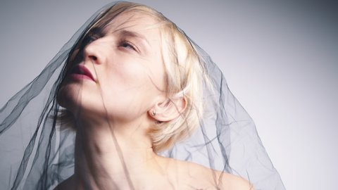 Fashion Model with a black net veil. Isolated woman under black cloth Net. Portrait of a blonde girl with serious facial expression.