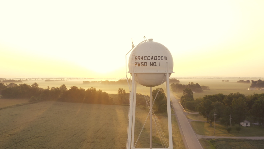 Aerial orbit of a water tower on farm land in Missouri with birds flying by.