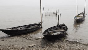 Lonely wooden fishing boats in the river. Three small fishing boats are waiting at the Padma river water in the autumn morning. Slow motion video. 