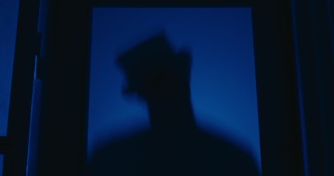 silhouette of a man with a top hat creeping on a glass door with blue light in the background