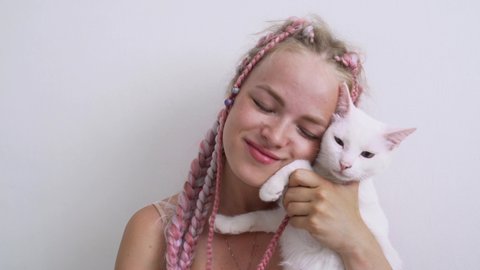Portrait blonde woman with afro haircut stroking white soft purebred cat at home sitting on cozy sofa hugs her beloved soft pet feels enjoying rest, close up.