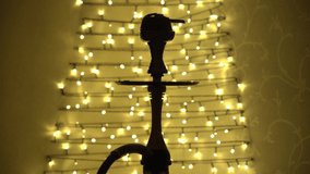 Video of close up view of hookah with blowing smoke with garlands backlight