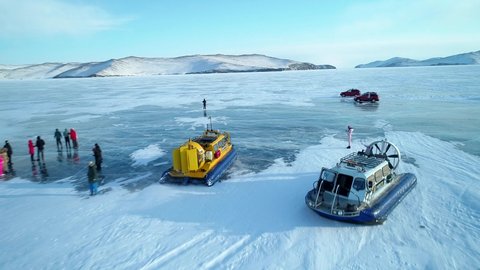 Khuzhir, Russia - February 27, 2021: Aerial view on the popular tourist spot, people travel around the frozen lake Baikal by hovercraft. Hovercraft departure. Transparent cracked ice. Amazing winter