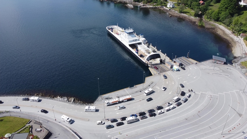 Car and passenger ferry Mf Oppdeal loading and discharging cars to road E39 at Lavik harbour - Static aerial showing ferry with port and ferry queue - Norway Royalty-Free Stock Footage #1080780362