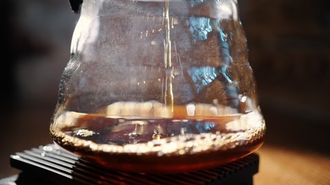 drip coffee brewing. rare video frame. close-up. freshly brewed coffee drips from paper filter into traditional drip brewing glass kettle, in a thin stream. with backlight
