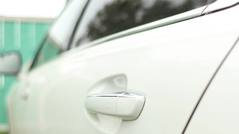 Close-up of a rear door handle of a car and a man opening the door gets behind the wheel on a blurred background
