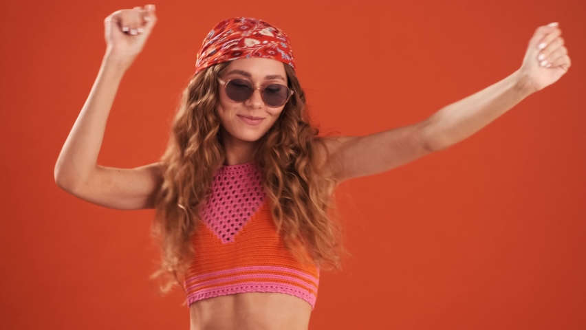 The smiling curly-haired woman with bandana on her head dancing in the orange studio