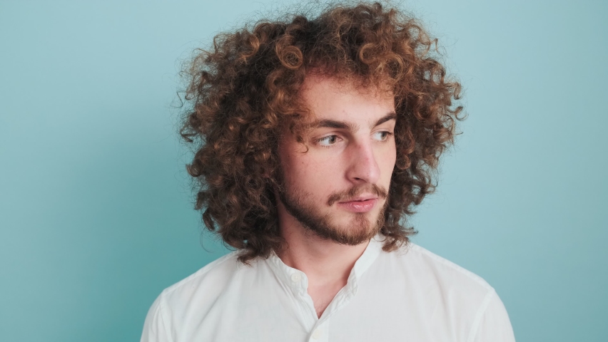 A curly man is doing silence gesture to the camera standing isolated over blue background