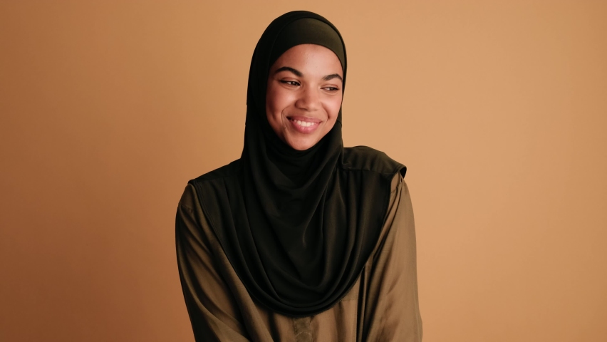 A laughing arabian woman is posing to the camera standing isolated over beige background